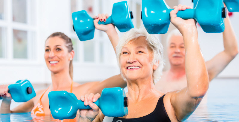 young and senior in water gymnastics physiotherapy with dumbbells