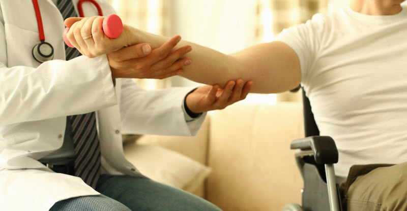 Male doctor helps lift dumbbell to disabled patient